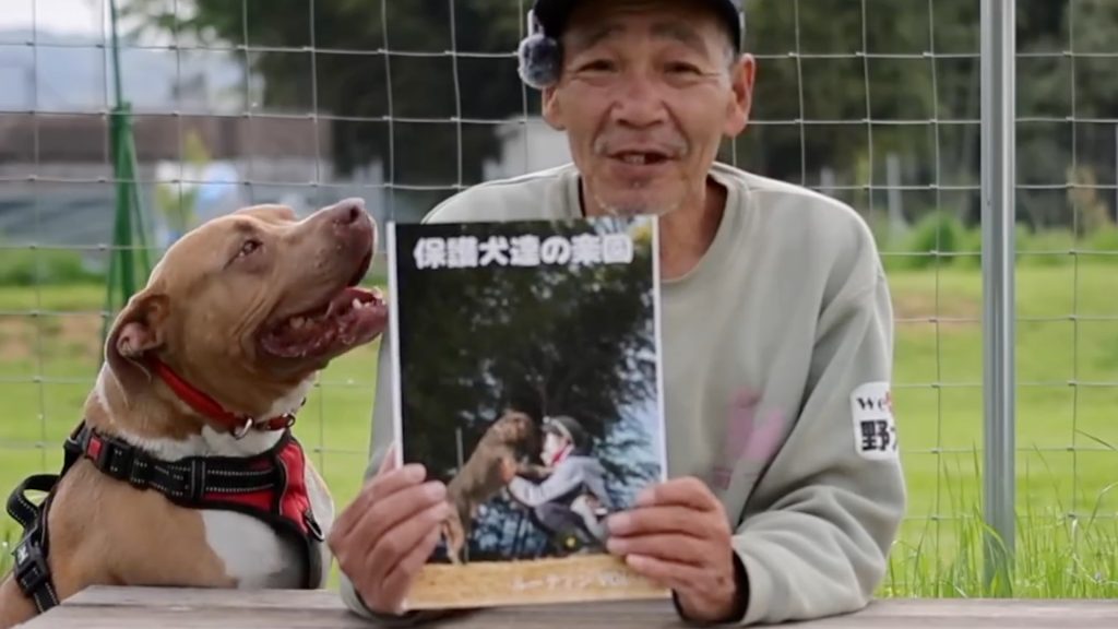 北村紋義（ポチパパ）さんと保護犬の写真3。写真集の第一弾を手にして